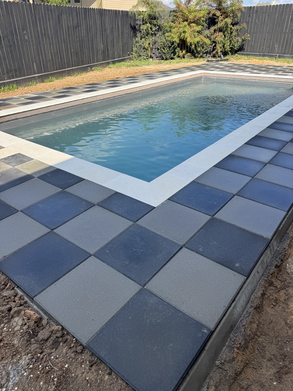 After view of a swimming pool surrounded by charcoal and gray square pavers
